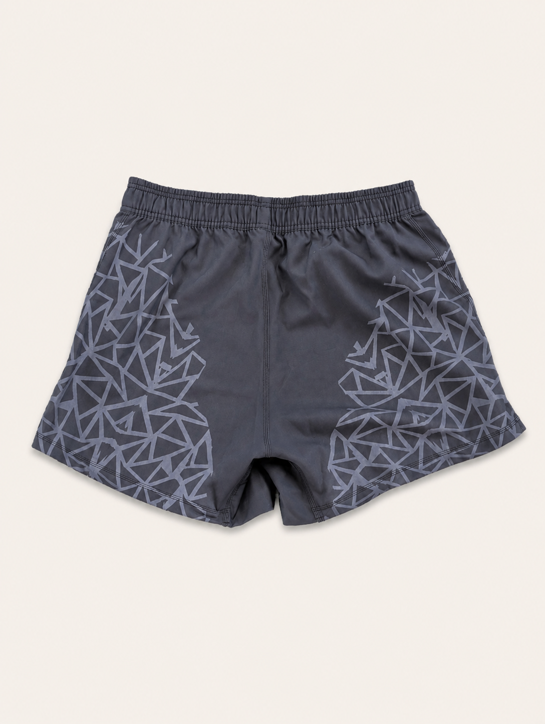 Dark gray athletic shorts with a light gray geometric triangle pattern on the sides, featuring an elastic waistband, shown flat on a light beige background.